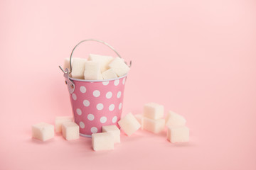 Sugar cubes in little bucket on pink background, sweet food