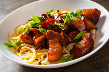 Boiled spaghetti with fried small pieces of meat on a wooden background