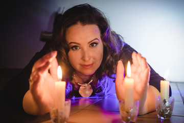 Portrait of adult girl with black hair and candles in the dark room