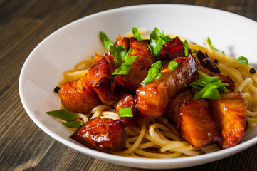 Boiled spaghetti with fried small pieces of meat on a wooden background