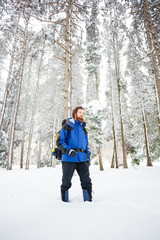 Young male mountain climber in blue and black clothing hiking toward camera through deep powder...