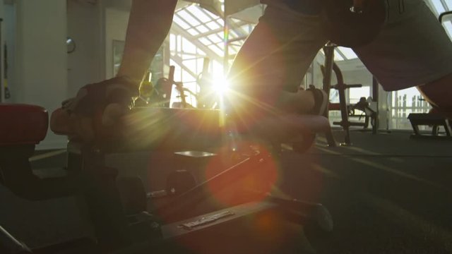 Tilt up of man training at the gym and using dumbbells, shot against the sun during sunset
