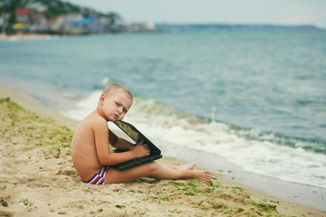 Fototapeta na wymiar Thoughtful little boy with laptop at sea coast