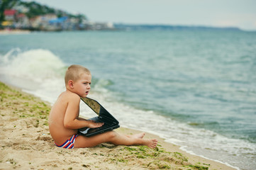 Fototapeta na wymiar Thoughtful little boy with laptop at sea coast