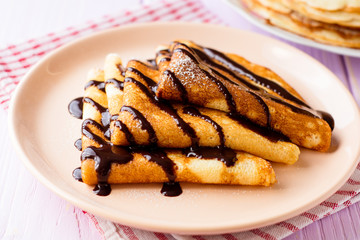 Crepes with chocolate syrup on purple wooden background.