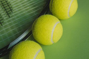 Three tennis balls and a tennis racket on green background. Close up.