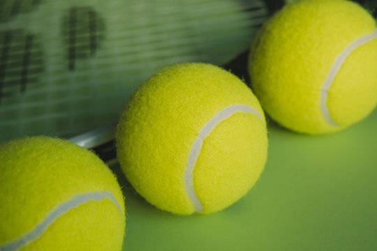 Macro view of three tennis balls and a tennis racket on green background.