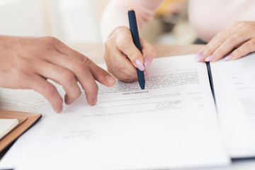 A couple of old people at a reception with a realtor. A woman in a pink sweater signs a contract with a realtor.