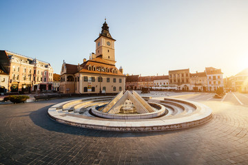 Obraz premium City central square (Piata Sfatului) with town council hall tower, fountain morning sunrise view, location Brasov, Transylvania, Romania. Famous travel destination summer postcard.