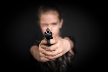Girl aiming a gun at the camera, blurred background, on black