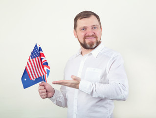 An adult bearded man holds flags of English-speaking countries in the UK, USA, Australia.