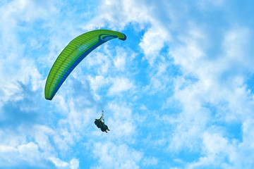 Landscape of mountains against the blue sky and white clouds. Sun rays. One paratrooper flying over the mountain massif against the blue sky 