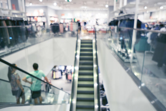 Blurred background of a modern shopping mall. Big sales on Black Friday for Christmas. Escalators. Blurred showcases fashion boutique with clothes. People make shopping