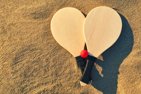 Set for a game of beach tennis close-up. Wooden rackets and red ball in the sand. Basic background for design.                             