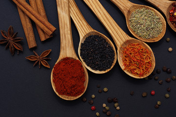 Fototapeta premium Spice. Spice in a wooden spoon. Herbs. Curry, saffron, turmeric, pepper and others on a black background.