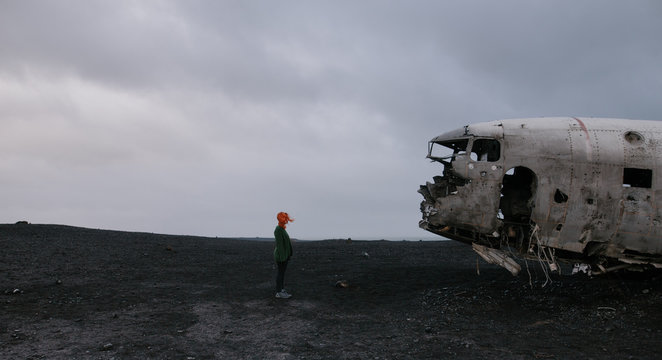 woman in front of the crashed Navy Douglas Super DC-3 plane in Vik, Iceland