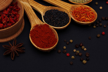 Fototapeta premium Spice. Spice in a wooden spoon. Herbs. Curry, saffron, turmeric, pepper and others on a black background.