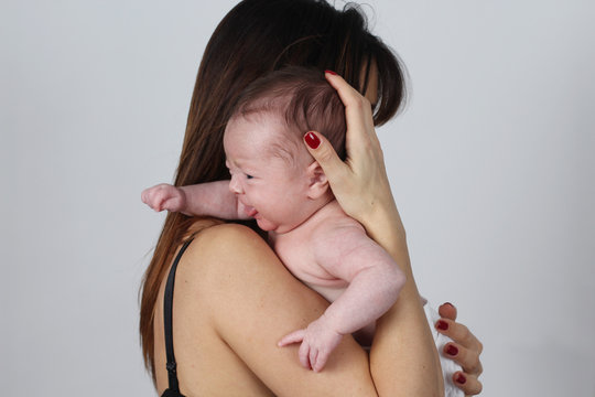 Young Mother Holding Her Crying Baby Daughter On Studio