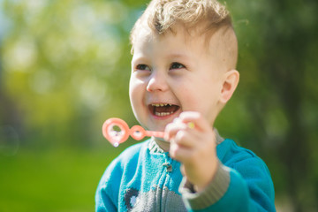 The boy blows out soap bubbles and laughs out loud. Happy child outdoors.