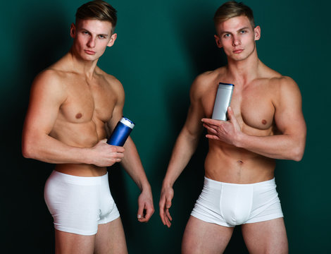Twin athletes with serious faces wear underwear and hold shampoo
