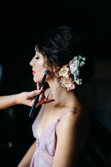 Brunette bride with red lips and flowers in her hair, powder brush near her face