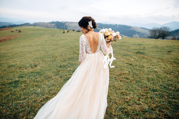 Fototapeta na wymiar The bride in beige dress with naked back are walking on green hill with mountains on background