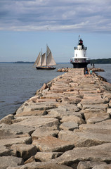 Schooner Sailboat Passes by Lighthouse Situated on Edge of Stone Jetty in Maine
