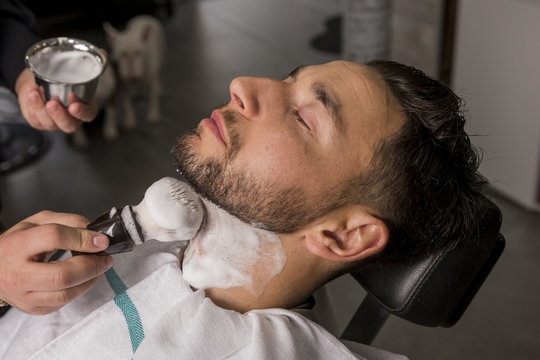 Hairdresser shaving his beard with a razor to a client