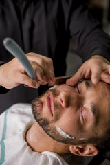 Hairdresser shaving his beard with a razor to a client
