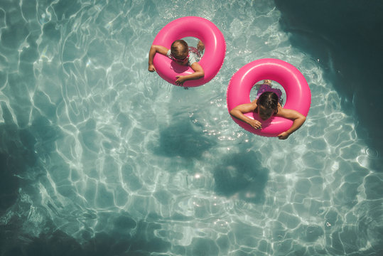 Two Girls Floating In a Blue Pool With Pink Floats
