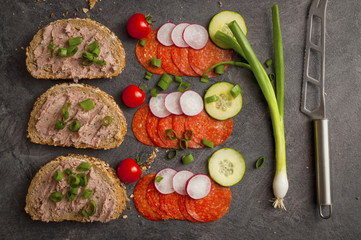sandwich with vegetables and salami on a black table, healthy food. 
