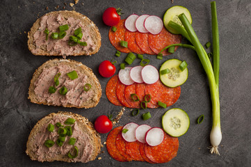 sandwich with vegetables and salami on a black table, healthy food. 