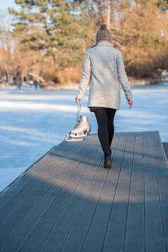 Young woman holding ice skates walking toward frozen lake