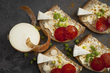 sandwich of spicy salami and cheese on a black wooden table.
