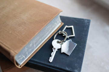 House key and keychain in the form of homes lies on books. Concept for real estate, mortgage, moving home or renting property.