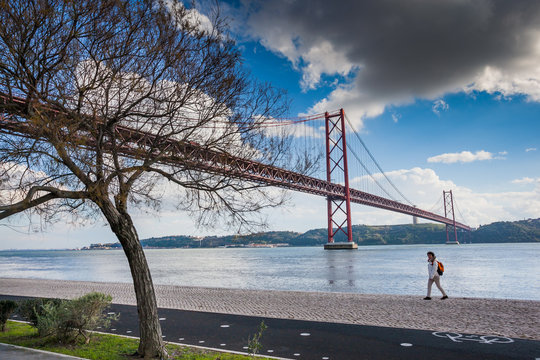 LISBON, PORTUGAL - January 28, 2011: A woman walks along the banks of Tagus River in Belem and famouse bridge of 25th April over river on January 28, 2011, Lisbon, Portugal