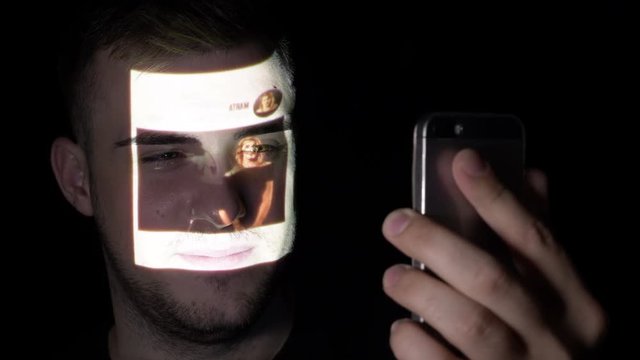 Young male freelancer searching people on social media using his smartphone while the images are projected on his face