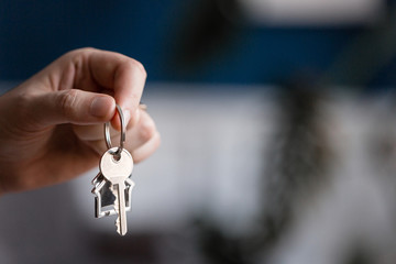 Mortgage concept. Men hand holding key with house shaped keychain. Modern light lobby interior....