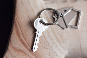 House key and keychain in the form of homes lies on wooden boards. Concept for real estate, mortgage, moving home or renting property.
