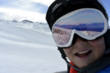 Happy cute boy in ski goggles is going  up the mountain on a ski lift