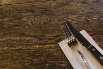 Knife and fork on a wood table with white napkin