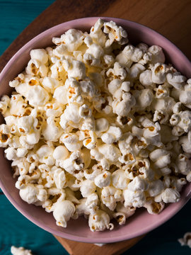 Popcorn in pink bowl on wooden board on dark green background