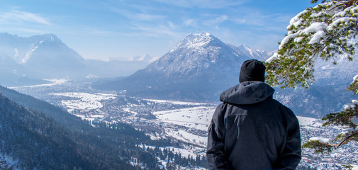 Fototapeta na wymiar Mann genießt die Aussicht und schaut herab auf Garmisch-Partenkirchen und Farchant
