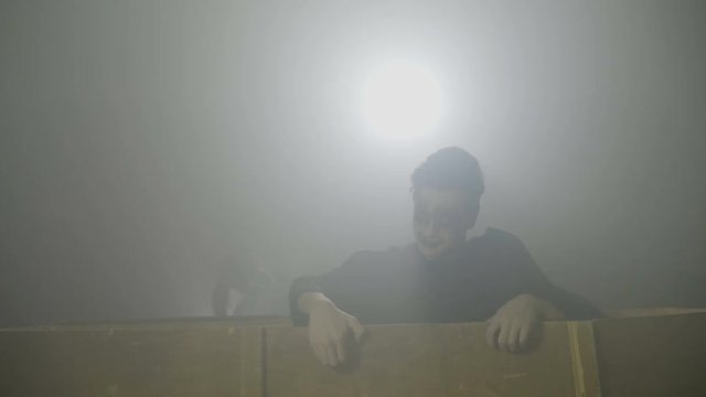 Couple of young zombies wearing frightening clothes waking up on day of the dead and getting out from their coffins in fog