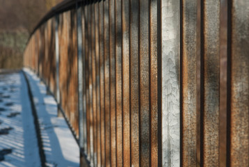Metal, rusty bridge railing covered in snow lit by morning sun