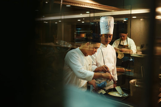 Trainee cooking with chef in kitchen