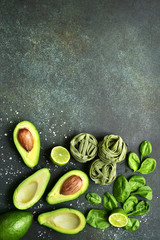 Uncooked spinach pasta (tagliatelle) and green vegetables (spinach, lime, avocado).Top view with copy space.