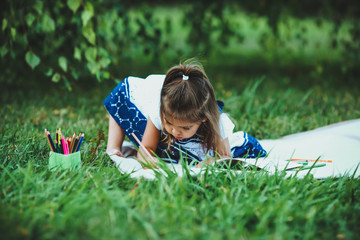 Happy little girl draws sitting on grass.