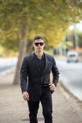 Good looking man in fashion shoot, wear black dress shirt and sunglasses walking on the street