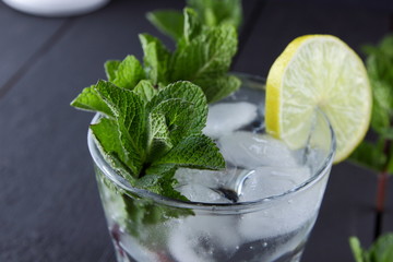 Mojito on a dark background, summer cocktail with lime and mint, refreshing drink with lemon, fresh mint for cocktail, celebratory drink with ice, copy space, minimalist cocktail